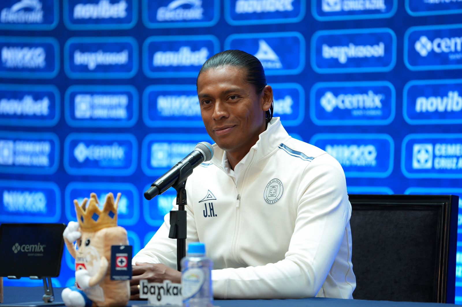 Joel Huiqui junto a un micrófono con chamarra blanca