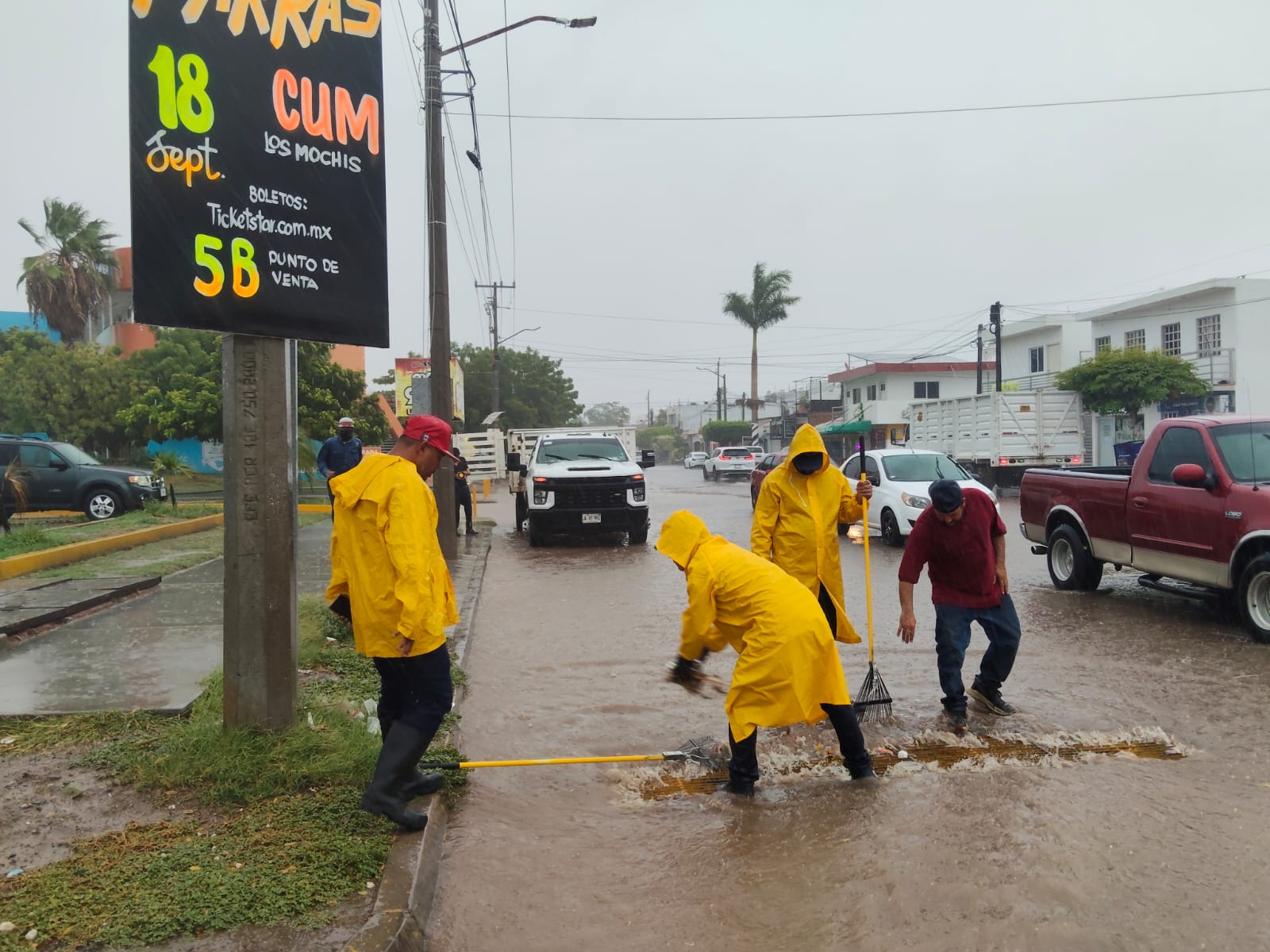 Personas con impermeable amarillo con una escoba y la calle inundada