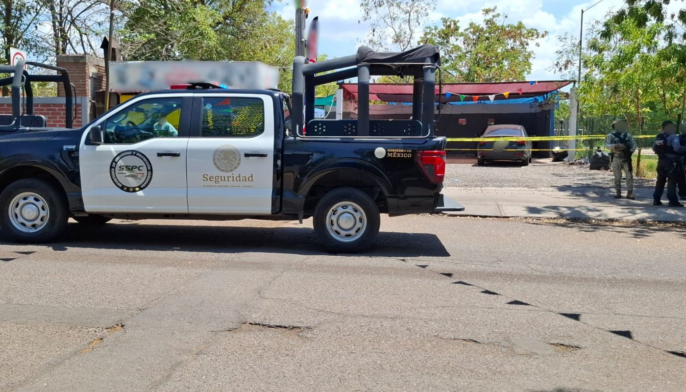 Unidad policiaca afuera de un establecimiento de lavado de autos, al extremo, tres elementos policiacos
