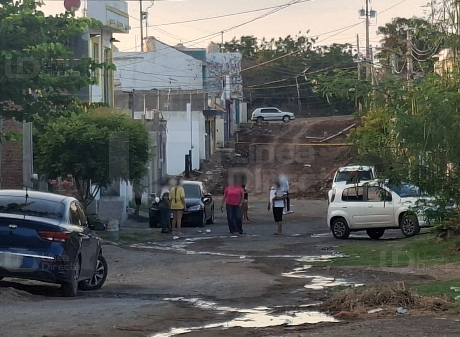 Unidades de corporaciones policiacas y carros particulares en una camino de terracería con cintas amarillas de precaución y al fondo casas