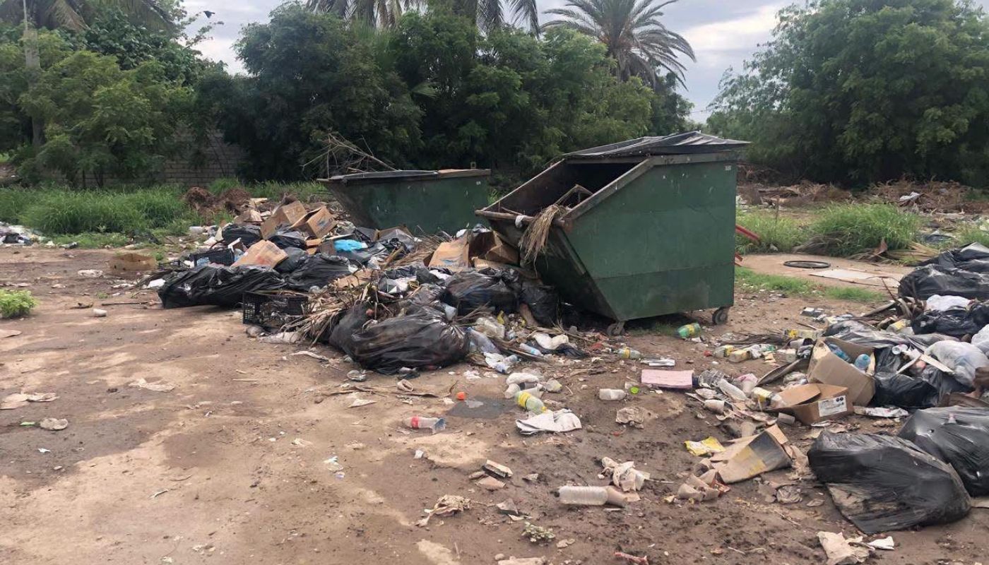 contenedores de basura y basiura esparcida en un baldío