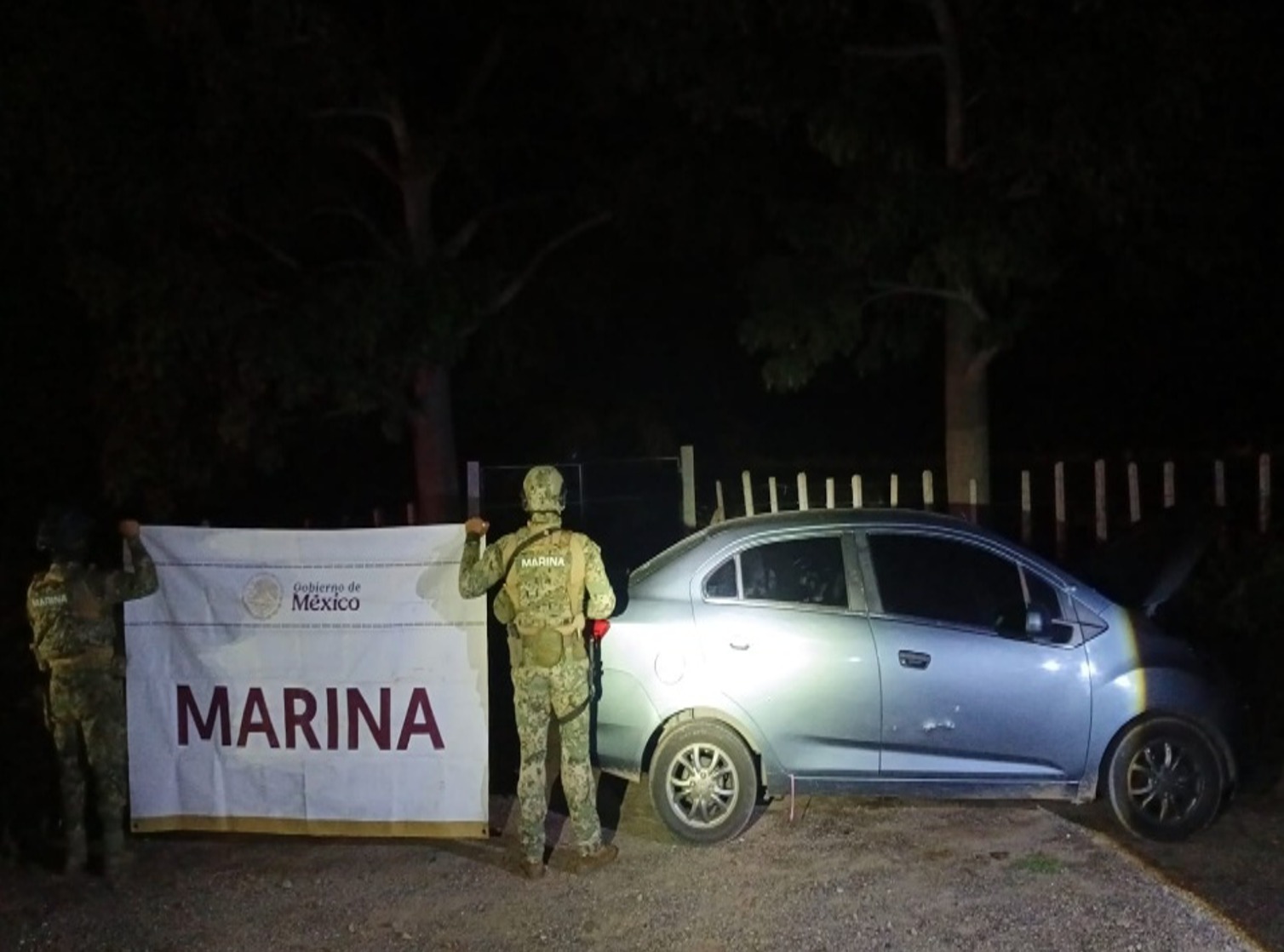 elementos militares sosteniendo una lona a lado de un vehículo de color gris