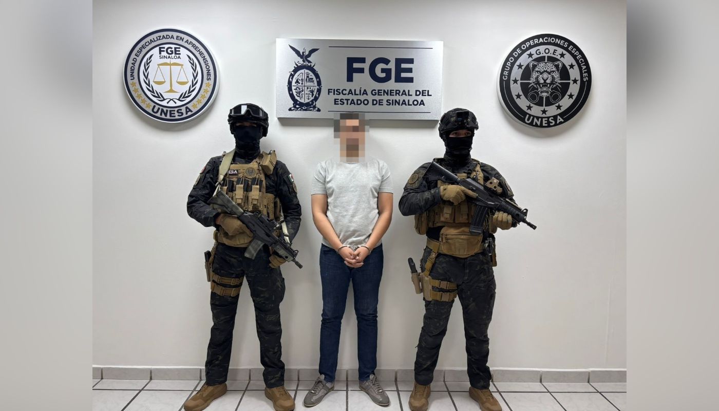 Civil con las manos esposadas al frente y el rostro cubierto y a las orillas, dos elementos policiacos con armas