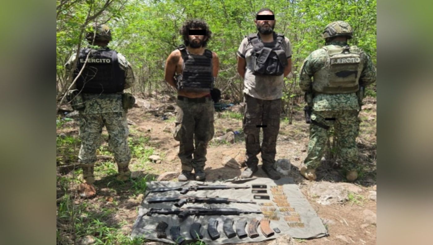 dos civiles con el rostro cubierto y las manos atadas en medio de dos agentes del Ejercito en una zona de bosque