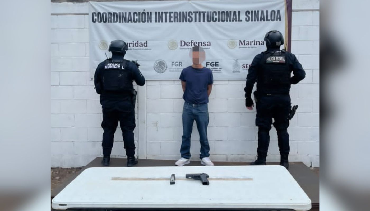 Persona detenida junto a dos elementos de seguridad y al frente una mesa con un arma