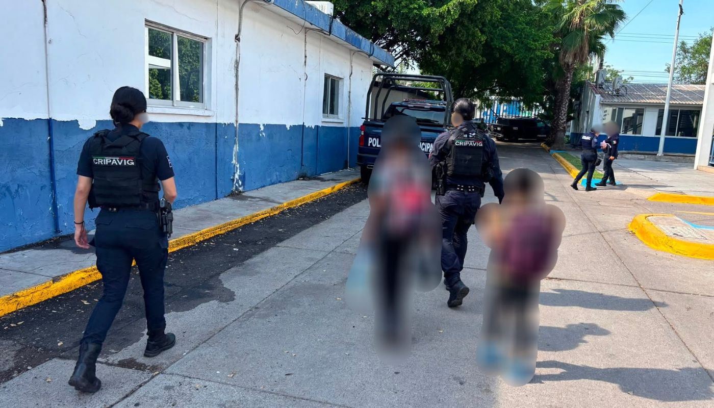 Agentes policiacos caminando junto a dos niñis en una institución